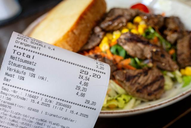 ILLUSTRATION - 15 April 2025, Bremen: A restaurant bill with VAT is seen next to a full plate on a table. Revenues in the German hospitality industry dropped 3.5% in August, the high season for tourism, a report from the Federal Statistical Office revealed on Tuesday. Photo: Sina Schuldt/dpa