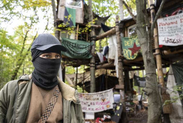 21 October 2025, Hesse, Langen: A masked activist stands in front of a tree house near the Langener Waldsee lake. Environmentalists have been protesting here for months against the planned clearing of the area where gravel is to be mined in the future. Photo: Boris Roessler/dpa