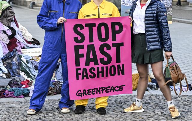 22 October 2025, Berlin: A fashionably dressed woman poses for a photo with a "Stop Fast Fashion" sign during a protest organized by environmental group Greenpeace in front of the Brandenburg Gate. The activists are calling for an anti-fast fashion law. Photo: Jens Kalaene/dpa
