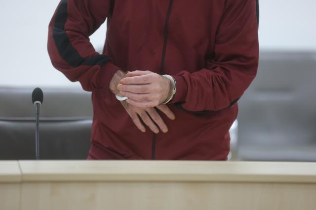 23 October 2025, Thuringia, Gera: The defendant stands in the courtroom  in handcuffs. The 46-year-old man is accused of pouring petrol over his wife in a streetcar and then setting her on fire in a tram in the central German city of Gera. Photo: Bodo Schackow/dpa
