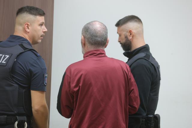 23 October 2025, Thuringia, Gera: The defendant (C) is led into the courtroom by court officials. The 46-year-old man is accused of pouring petrol over his wife in a streetcar and then setting her on fire in a tram in the central German city of Gera. Photo: Bodo Schackow/dpa