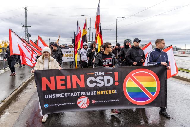 25 October 2025, Brandenburg, Cottbus: People take part in a counter-demonstration to Christopher Street Day (CSD), carrying Young Nationalists flags, German flags and Reich flags, as they walk past the GladHouse youth center, where a rainbow flag hangs Photo: Frank Hammerschmidt/dpa