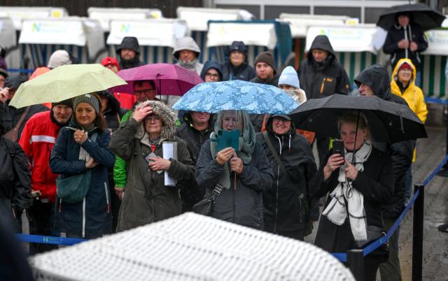 25 October 2025, North Rhine-Westphalia, Norden-Norddeich: Despite the rain, bidders gather in front of the stage for a beach chair auction. As the tourist season comes to an end, numerous bargain hunters take the opportunity to buy discarded beach chairs in the East Frisian coastal town of Norddeich. Photo: Lars Penning/dpa