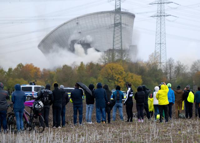 25 October 2025, Bavaria, Gundremmingen: People watch as the second cooling tower of the decommissioned Gundremmingen nuclear power plant collapses after blasting. The two approximately 160-metre-high cooling towers of the nuclear power plant, which was shut down almost four years ago, were to be blown up today. Photo: Sven Hoppe/dpa