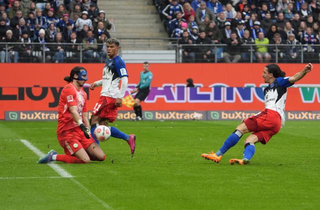 25 October 2025, Hamburg: Wolfsburg goalkeeper Kamil Grabara (L) defends a shot from Hamburger's Rayan Philippe during the German Bundesliga soccer match between Hamburger SV and VfL Wolfsburg at the Volksparkstadion. Photo: Marcus Brandt/dpa - IMPORTANT NOTICE: DFL and DFB regulations prohibit any use of photographs as image sequences and/or quasi-video.