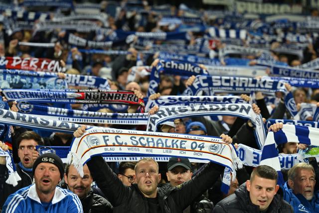 FILED - 17 October 2025, Lower Saxony, Hanover: Schalke fans celebrate with their scarves in the stands. after the German 2. Bundesliga soccer match between Hannover 96 - FC Schalke at Heinz von Heiden-Arena. Schalke fans are dreaming of a Bundesliga return after a strong start has moved them to the top of the second division. Photo: Swen Pförtner/dpa - IMPORTANT NOTE: In accordance with the regulations of the DFL German Football League and the DFB German Football Association, it is prohibited to utilize or have utilized photographs taken in the stadium and/or of the match in the form of sequential images and/or video-like photo series.