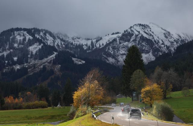 26 October 2025, Bavaria, Bad Hindelang: Cars drive through the autumn landscape in the sunshine in front of snow-covered mountains. Photo: Karl-Josef Hildenbrand/dpa