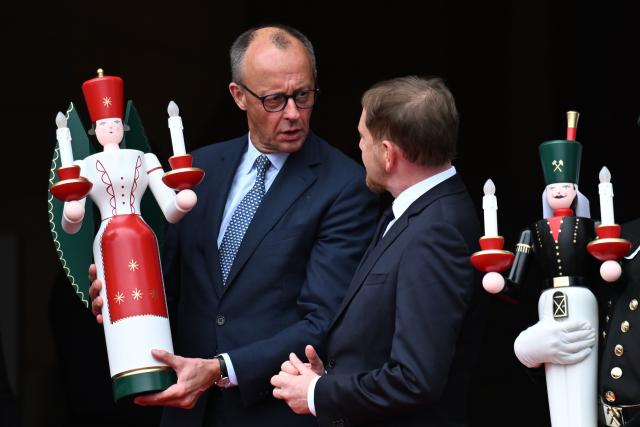 28 October 2025, Saxony, Dresden: German Chancellor Friedrich Merz (C) receives a figurine of an angel from the Ore Mountains, next to Michael Kretschmer Minister President of Saxony, in front of Saxony State Chancellery. Photo: Hendrik Schmidt/dpa