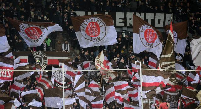 28 October 2025, Hamburg: St. Pauli fans wave flags during the German DFB Cup second-round soccer match between FC St. Pauli and TSG Hoffenheim at Millerntor-Stadion. Photo: Daniel Bockwoldt/dpa - WICHTIGER HINWEIS: Gemäß den Vorgaben der DFL Deutsche Fußball Liga bzw. des DFB Deutscher Fußball-Bund ist es untersagt, in dem Stadion und/oder vom Spiel angefertigte Fotoaufnahmen in Form von Sequenzbildern und/oder videoähnlichen Fotostrecken zu verwerten bzw. verwerten zu lassen.