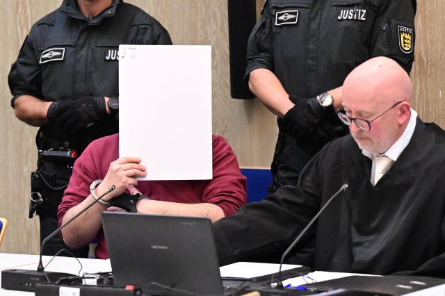 31 October 2025, Baden-Wuerttemberg, Mannheim: The defendant in a murder trial following a death drive from Mannheim sits in the courtroom with a file cover in front of his face, his defense lawyer Uwe Kosmala sits to his right. According to the public prosecutor's office, a man deliberately drove towards people during the drive at the beginning of March. An 83-year-old woman and a 54-year-old man were killed. 14 people were injured, five of them seriously. Photo: Bernd Weißbrod/dpa