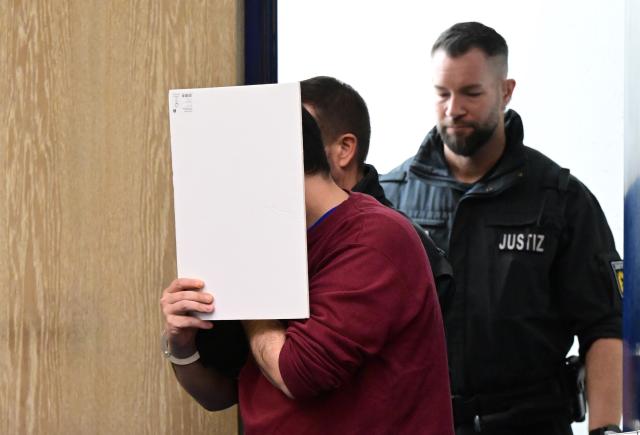 31 October 2025, Baden-Wuerttemberg, Mannheim: The defendant in a murder trial following a death drive from Mannheim enters the courtroom with a file cover in front of his face. According to the public prosecutor's office, a man deliberately drove towards people during the drive at the beginning of March. An 83-year-old woman and a 54-year-old man were killed. 14 people were injured, five of them seriously. Photo: Bernd Weißbrod/dpa