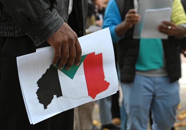 31 October 2025, Berlin: A person holds a flyer with the Sudanese flag during a vigil under the motto "Stand with Sudan - Stop the massacres in Al-Fasher" in front of the Federal Foreign Office. Photo: Elisa Schu/dpa