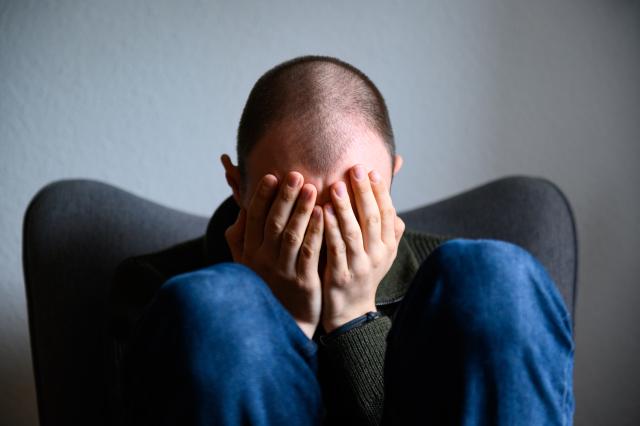 FILED - 18 February 2023, Hamburg: A man sits huddled on a chair with his hands in front of his face. A recent American scientific study revealed that receiving psychotherapy sessions via text message exchange between the patient and the psychiatrist helps in treating cases of mild depression. Photo: Jonas Walzberg/dpa