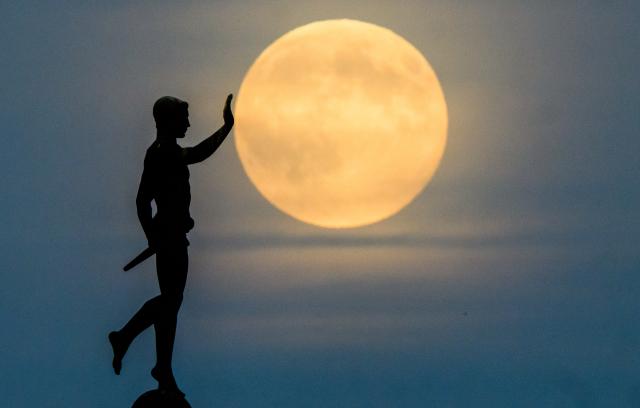 05 November 2025, Lower Saxony, Hanover: The moon rises on the horizon behind the "Torchbearer" statue on the northern shore of the Maschsee in Hanover. Photo: Julian Stratenschulte/dpa
