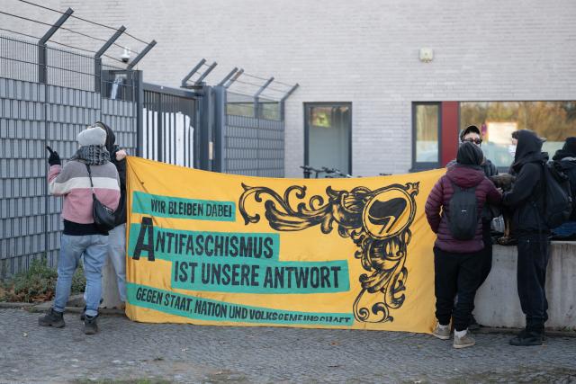 06 November 2025, Saxony, Dresden: Participants in a rally stand in front of the Higher Regional Court (OLG) with a banner reading "We are sticking to it - anti-fascism is our answer." The rally marks the start of the trial against an alleged confidant of NSU terrorist Beate Zschaepe, accused of supporting a terrorist organization, among other charges. Photo: Sebastian Kahnert/dpa