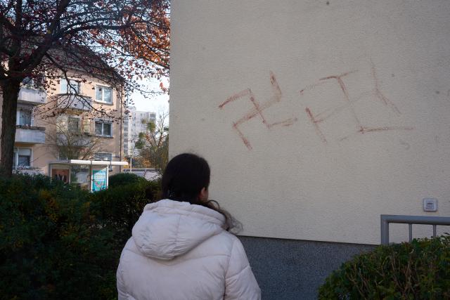 06 November 2025, Hesse, Hanau: A passer-by looks at swastikas that have obviously been smeared in blood on a house wall. Almost 50 cars, several letterboxes and house walls have been graffitied in Hanau. According to the police, the background and intentions of the person or persons behind this are still unclear. Photo: Thomas Frey/dpa