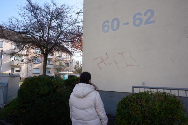 06 November 2025, Hesse, Hanau: A passer-by looks at swastikas that have obviously been smeared in blood on a house wall. Almost 50 cars, several letterboxes and house walls have been graffitied in Hanau. According to the police, the background and intentions of the person or persons behind this are still unclear. Photo: Thomas Frey/dpa