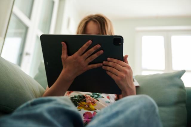 FILED - 28 May 2022, Berlin: A girl sits holds a tablet on the couch. Denmark is set to introduce a national minimum age of 15 for access to certain social media platforms, the government announced on Friday. Photo: Annette Riedl/dpa