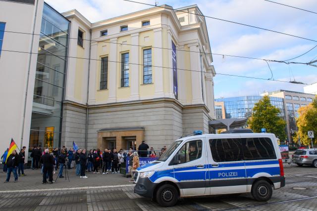 09 November 2025, Saxony-Anhalt, Magdeburg: A police vehicle drives past a demonstration in front of Magdeburg Opera House against the planned play "3 Minutes", which is to be based on the attack on Magdeburg's Christmas market in December 2024. Photo: Klaus-Dietmar Gabbert/dpa