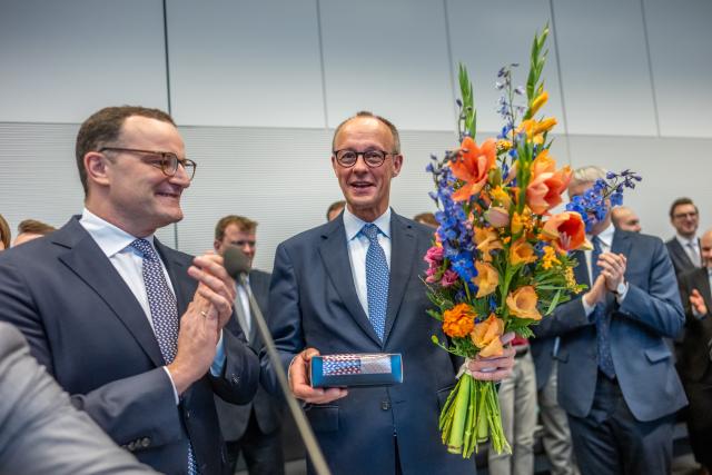 11 November 2025, Berlin: German Chancellor Friedrich Merz holds flowers he received for his 70th birthday next to Jens Spahn (L), Christian Democratic Union (CDU)/Chrisitan Social Union (CSU) parliamentary group leader, at the start of the parliamentary group meeting at the German Bundestag. Photo: Michael Kappeler/dpa
