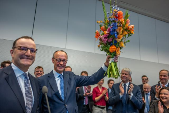 11 November 2025, Berlin: German Chancellor Friedrich Merz holds flowers he received for his 70th birthday next to Jens Spahn (L), Christian Democratic Union (CDU)/Chrisitan Social Union (CSU) parliamentary group leader, at the start of the parliamentary group meeting at the German Bundestag. Photo: Michael Kappeler/dpa