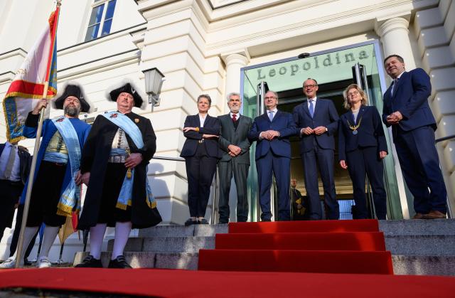18 November 2025, Saxony-Anhalt, Halle: German Chancellor Friedrich Merz (3rd R) is welcomed during his inaugural visit by Minister President of Saxony-Anhalt Reiner Haseloff (4th R), Minister for Infrastructure and Digital Affairs and Second Deputy Minister President of Saxony-Anhalt Lydia Hueskens (L), Saxony-Anhalt Minister of Economics Armin Willingmann, President of the National Academy of Sciences Leopoldina Bettina Rockenbach (2nd R) and Saxony-Anhalt Minister of Agriculture Sven Schulze in front of the National Academy of Sciences Leopoldina. Photo: Robert Michael/dpa
