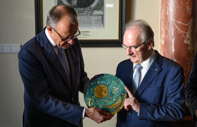 18 November 2025, Saxony-Anhalt, Halle: German Chancellor Friedrich Merz (L) receives a copy of the Nebra Sky Disk from Minister President of Saxony-Anhalt Reiner Haseloff during his inaugural visit to the National Academy of Sciences Leopoldina. Photo: Robert Michael/dpa
