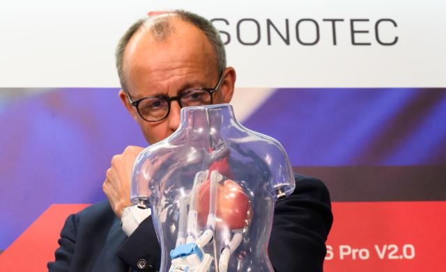18 November 2025, Saxony-Anhalt, Halle: German Chancellor Friedrich Merz looks at a model of an ultrasound sensor in children with heart disease during his inaugural visit to the company Sonotec Ultraschallensorik Halle GmbH in Saxony-Anhalt. Photo: Robert Michael/dpa