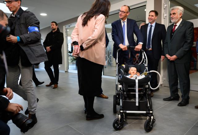 18 November 2025, Saxony-Anhalt, Halle: German Chancellor Friedrich Merz (C) stands by a baby carriage with a model for the use of an ultrasound sensor in children with heart disease during his inaugural visit to the company Sonotec Ultraschallensorik Halle GmbH in Saxony-Anhalt. Photo: Robert Michael/dpa