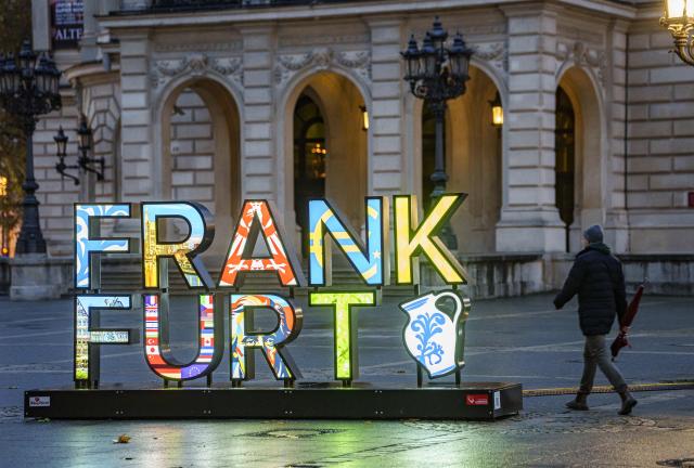 19 November 2025, Hesse, Frankfurt/Main: A man walks past the "Frankfurt Selfie Point" in front of the Alte Oper with an umbrella. Hesse is still expecting cold and wet winter weather in the coming days. Photo: Andreas Arnold/dpa