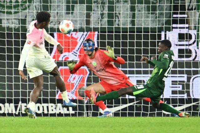 22 November 2025, Wolfsburg: Bayer Leverkusen's Ernest Poku in action against Wolfsburg goalkeeper Kamil Grabara and Sael Kumbedi during the German Bundesliga soccer match between VfL Wolfsburg and Bayer Leverkusen at the Volkswagen Arena. Photo: Swen Pförtner/dpa - IMPORTANT NOTICE: DFL and DFB regulations prohibit any use of photographs as image sequences and/or quasi-video.