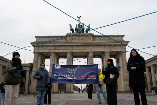 25 November 2025, Berlin: People hold a net made of purple threads in front of the Brandenburg Gate during a rally. Behind them are people holding a poster with the words "Live free - without violence". Actions take place in Berlin to mark the International Day against Violence against Women. Photo: Markus Lenhardt/dpa
