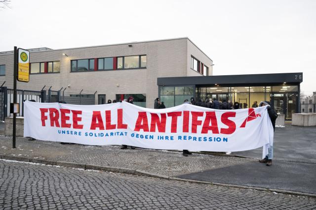 25 November 2025, Saxony, Dresden: Participants in a rally stand in front of the Dresden Higher Regional Court (OLG) holding a banner reading "Free All Antifas". The occasion is a trial against seven suspected left-wing extremists who are accused of membership of a criminal organization, among other things. Photo: Sebastian Kahnert/dpa