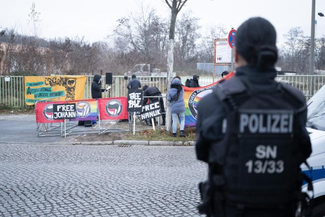 25 November 2025, Saxony, Dresden: A policewoman observes participants at a rally in front of the Dresden Higher Regional Court (OLG). The occasion is a trial against seven suspected left-wing extremists who are accused of membership of a criminal organization, among other things. Photo: Sebastian Kahnert/dpa