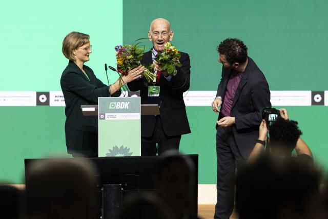 29 November 2025, Lower Saxony, Hanover: Federal chairmen of of Alliance 90/The Greens Franziska Brantner (L) and Felix Banaszak (R) present flowers to Former Israeli Prime Minister Ehud Olmert during the federal party conference of of Alliance 90/The Greens. Photo: Michael Matthey/dpa