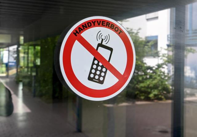 FILED - 22 August 2022, Berlin: A "no cell phones" sign is posted at the entrance to a school in Neukoelln. Singapore's Ministry of Education has announced that, starting in January 2026, high school students will be prohibited from using smartphones or smartwatches even outside of class time, such as during breaks and extracurricular activities, as part of stricter guidelines on electronic device use. Photo: Jens Kalaene/dpa
