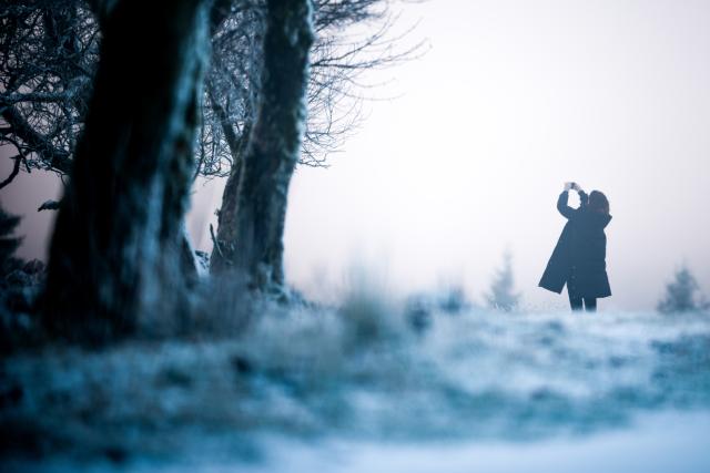 01 December 2025, North Rhine-Westphalia, Winterberg: A woman takes a photo with her smartphone in the snow on the Kahler Asten in the Sauerland. Photo: Christoph Reichwein/dpa