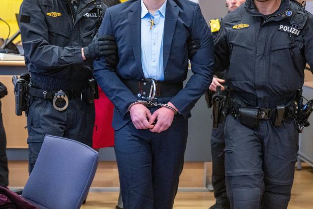 01 December 2025, Bavaria, Regensburg: Police officers lead a defendant into the district court courtroom. According to the indictment, on August 17, 2024, four men overpowered a district hospital employee to force open a gate and then fled the facility. Photo: Armin Weigel/dpa