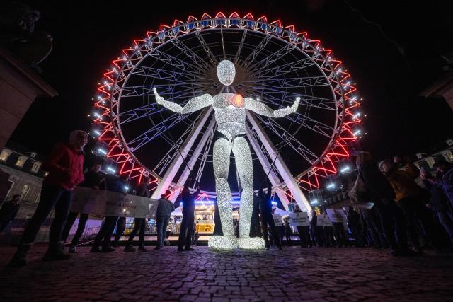 01 December 2025, Baden-Württemberg, Stuttgart: The eight meter high illuminated puppet "Vektor" from the large puppet theater "Dundu" is led by puppeteers in front of the Ferris wheel at the New Palace in Stuttgart. The performance of the large puppet accompanied a campaign by AIDS-Hilfe Stuttgart to mark World AIDS Day. Photo: Marijan Murat/dpa