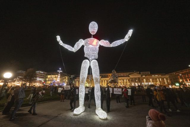 01 December 2025, Baden-Württemberg, Stuttgart: The eight meter high illuminated puppet "Vektor" from the large puppet theater "Dundu" is led by puppeteers around the Christmas market in Stuttgart. The performance of the large puppet accompanied a campaign by AIDS-Hilfe Stuttgart to mark World AIDS Day. Photo: Marijan Murat/dpa