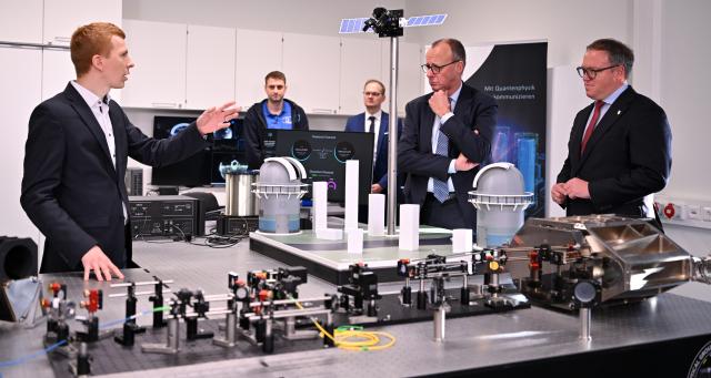 02 December 2025, Thuringia, Jena: A researcher (L) shows Mario Voigt (R), Minister President of Thuringia, and Germany's Chancellor Friedrich Merz (2nd R) a laboratory at the Fraunhofer Institute for Applied Optics and Precision Engineering during their inaugural visit to Thuringia. Photo: Martin Schutt/dpa
