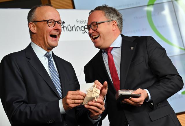 02 December 2025, Thuringia, Jena: Mario Voigt (R), Minister President of Thuringia, and Germany's Chancellor Friedrich Merz share a light moment during their inaugural visit to the Fraunhofer Institute for Applied Optics and Precision Engineering in Thuringia. Photo: Martin Schutt/dpa