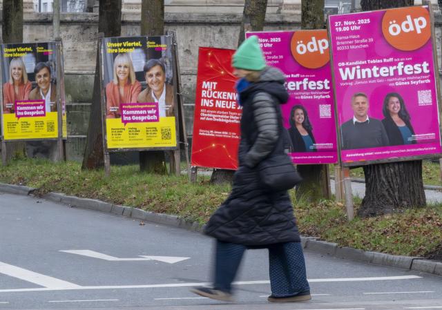 02 December 2025, Bavaria, Munich: A woman walks past various posters for the Bavarian local elections on Europaplatz. Photo: Peter Kneffel/dpa - ACHTUNG: Nur zur redaktionellen Verwendung im Zusammenhang mit der aktuellen Berichterstattung über die Bayerische Kommunalwahl 2025 und nur mit vollständiger Nennung des vorstehenden Credits