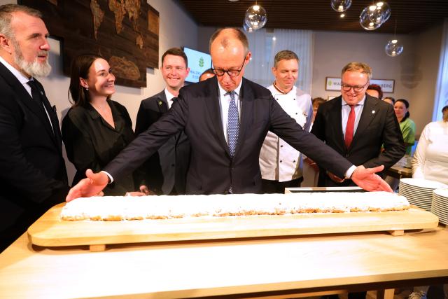 02 December 2025, Thueringen, Eisenberg: German Chancellor Friedrich Merz (C) and Mario Voigt (R), Minister President of Thuringia, cutting a stollen during a visit to the Waldkliniken Eisenberg on the occasion of his inaugural visit to Thuringia. Photo: Bodo Schackow/dpa