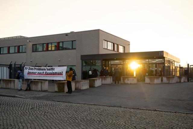 03 December 2025, Saxony, Dresden: Participants in a rally stand in front of the Higher Regional Court (OLG) holding a banner reading 'The problem is still racism,' as a trial begins against an alleged confidante of NSU terrorist Beate Zschaepe. Photo: Sebastian Kahnert/dpa