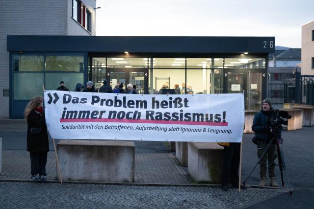 03 December 2025, Saxony, Dresden: Participants in a rally stand in front of the Higher Regional Court (OLG) holding a banner reading 'The problem is still racism,' as a trial begins against an alleged confidante of NSU terrorist Beate Zschaepe. Photo: Sebastian Kahnert/dpa