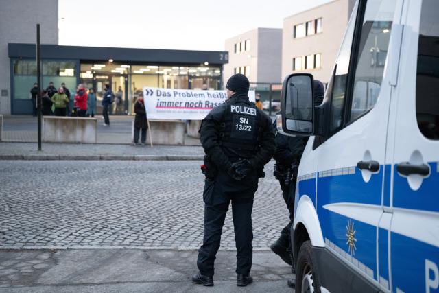 03 December 2025, Saxony, Dresden: Participants in a rally stand in front of the Higher Regional Court (OLG) holding a banner reading 'The problem is still racism,' as a trial begins against an alleged confidante of NSU terrorist Beate Zschaepe. Photo: Sebastian Kahnert/dpa