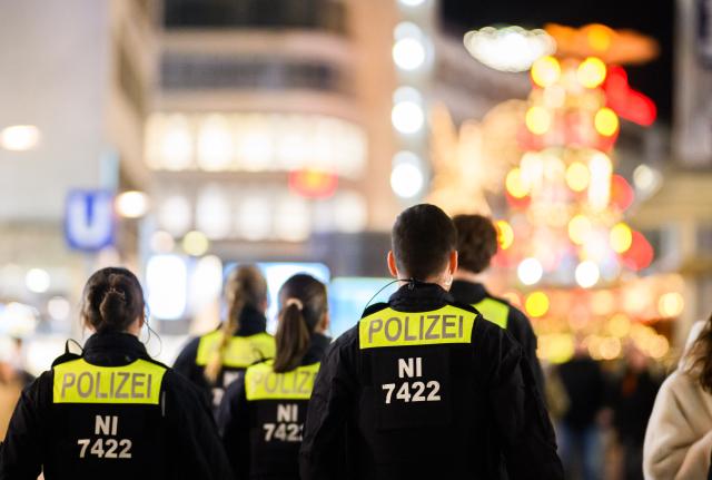 03 December 2025, Lower Saxony, Hanover: Police officers walk through the city center in front of the Christmas pyramid at Kroepcke. German Christmas markets are massively arming themselves after attacks in previous years. Photo: Julian Stratenschulte/dpa