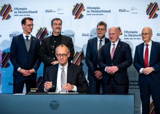 04 December 2025, Berlin: German Chancellor Friedrich Merz sits in front of (L-R), Hendrik Wuest, Minister President of North Rhine-Westphalia, Markus Soeder, Minister President of Bavaria and CSU Chairman, Thomas Weikert, President of the German Olympic Sports Confederation (DOSB), Kai Wegner, Governing Mayor of Berlin, and Peter Tschentscher, First Mayor of Hamburg, at the signing of the agreement on Germany's bid to host the Olympic Games in Germany. Photo: Michael Kappeler/dpa