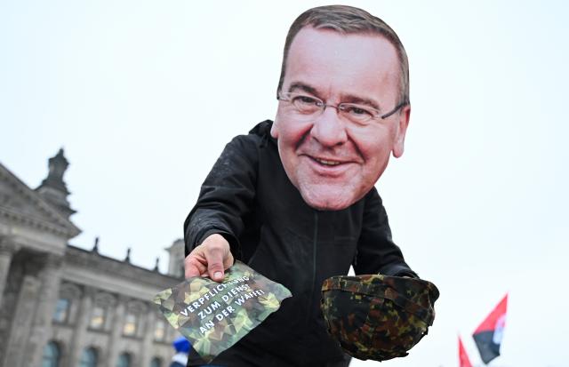 05 December 2025, Berlin: An activist dressed as German Defence Minister Boris Pistorius pulls a slip of paper reading 'Mandatory Military Service' from a helmet. The governing coalition plans a new military service law in response to the changed security situation, introducing compulsory conscription for entire year groups of young men and targets for expanding the Bundeswehr. Photo: Elisa Schu/dpa